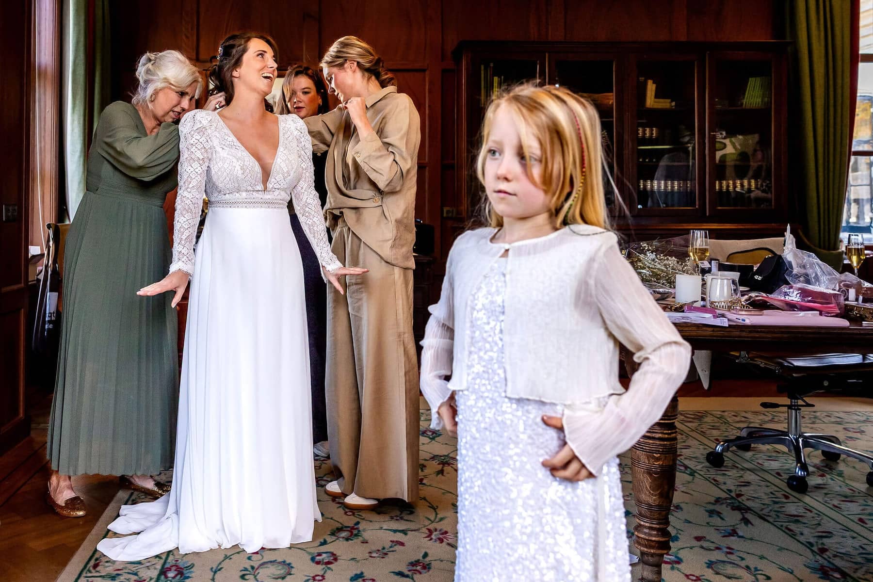 The bride getting dressed in a wood-panelled room, with a girl in a sparkly dress in the foreground