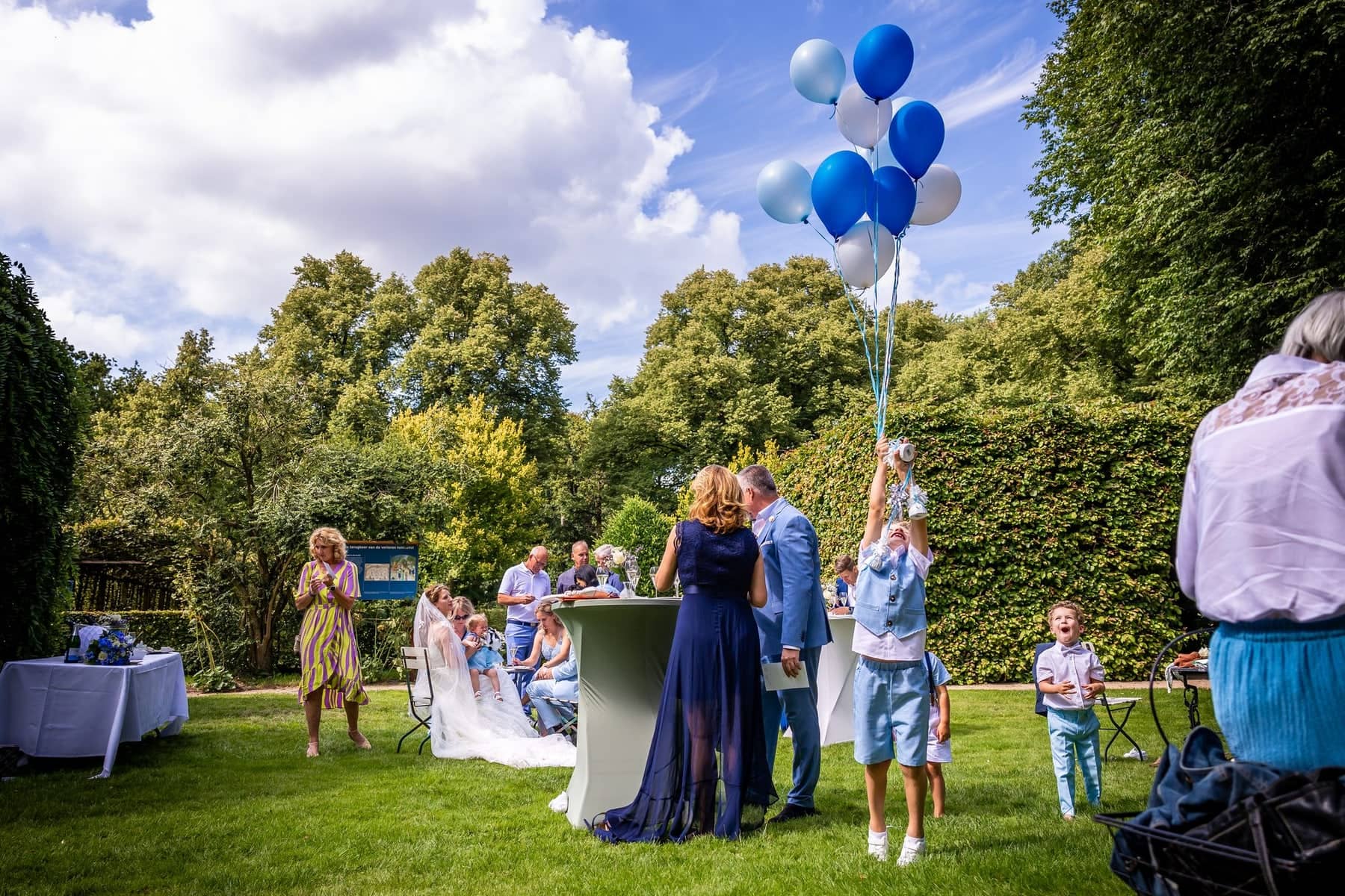 Reception in a sunny garden, a boy runs off with a bunch of blue balloons