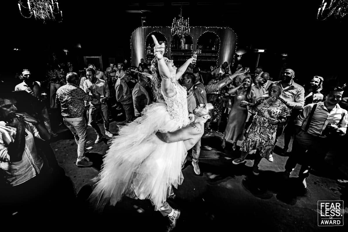 The bride dances with her arms in the air on a packed dance floor (black and white)