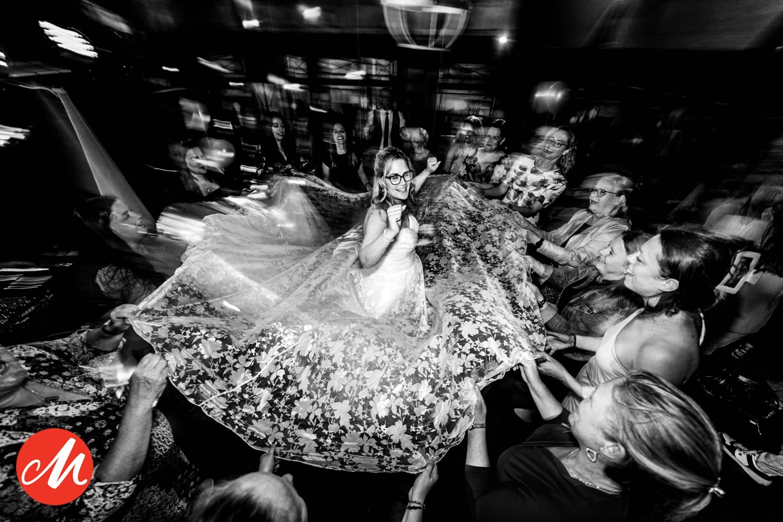 The bride spins among the guests, her dress fanning out (black and white)