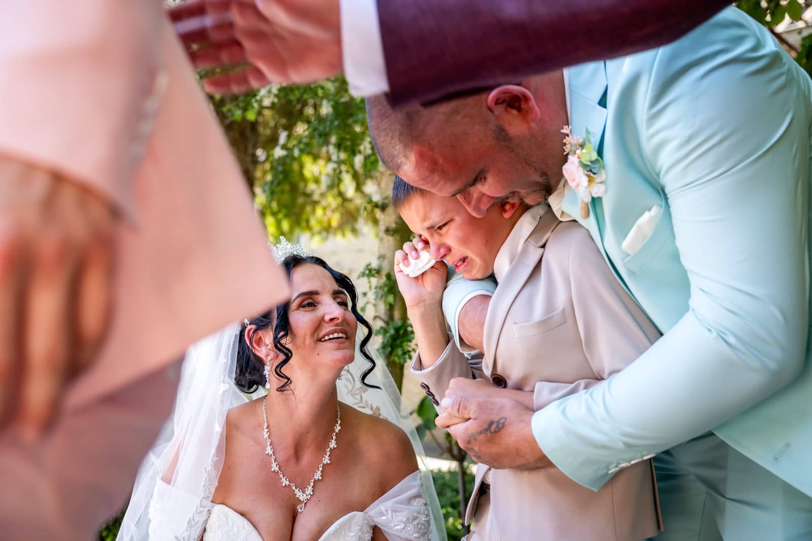 The bride looks on, beaming, as the groom hugs a tearful boy