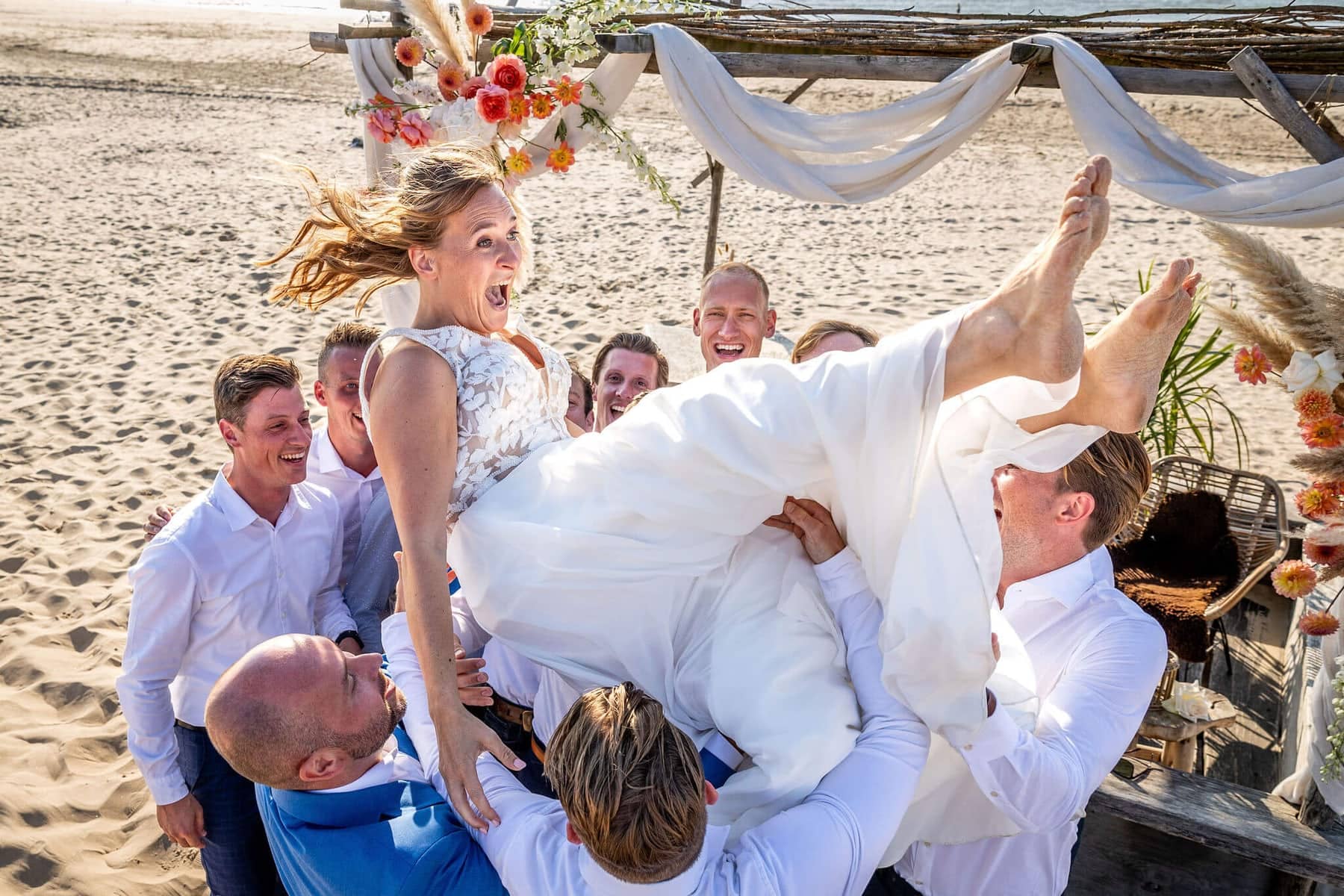 Friends lift the laughing bride into the air on the beach