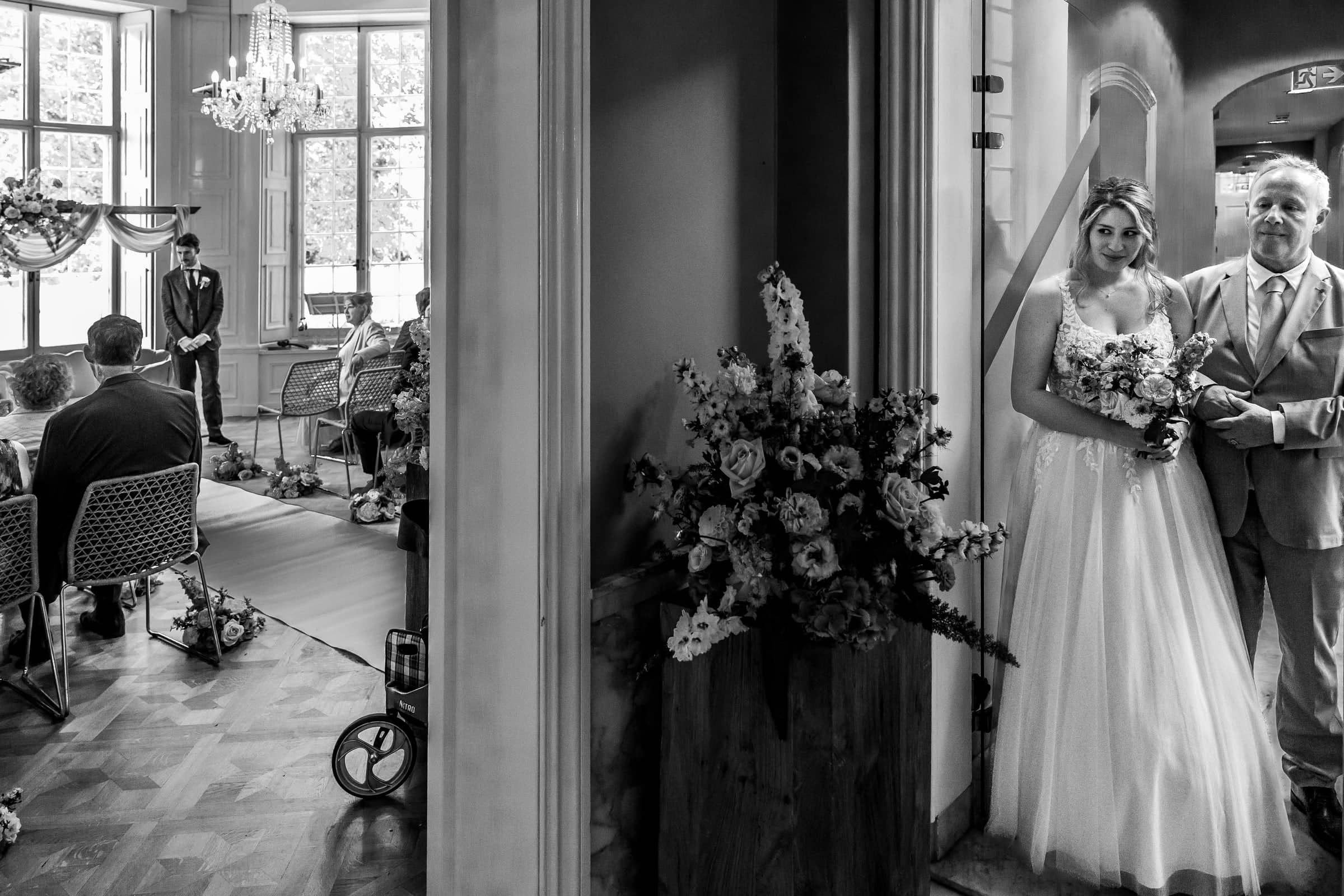 The bride and her father wait in the doorway before walking in (black and white)