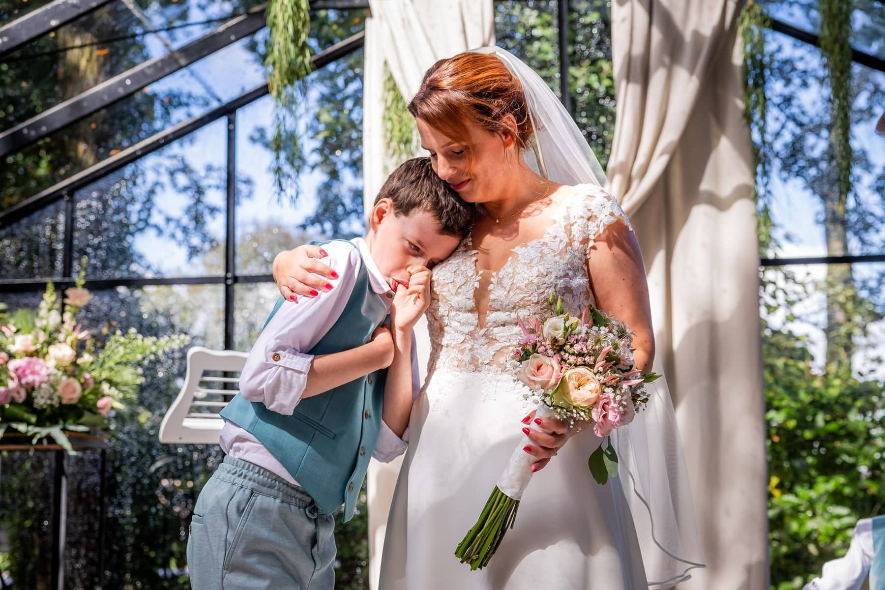 An emotional son hugs the bride during the ceremony in the glasshouse