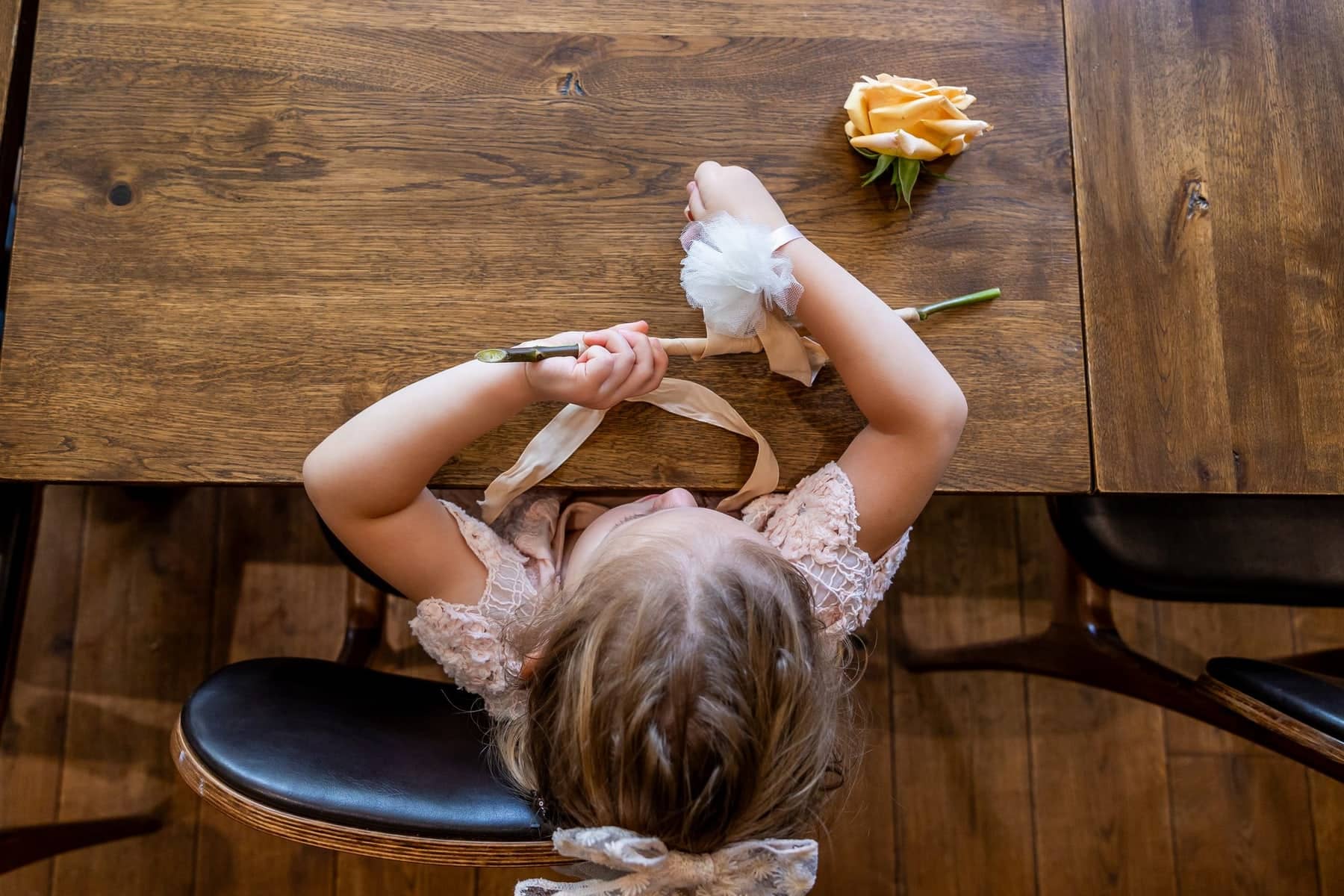From above: a flower girl at a wooden table with a rose and her flower wand