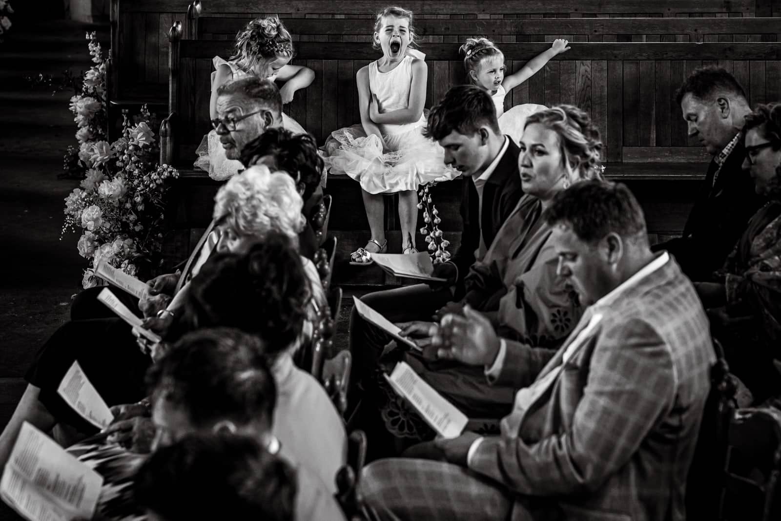 During the ceremony the flower girls yawn and jump on the bench while guests read along (black and white)
