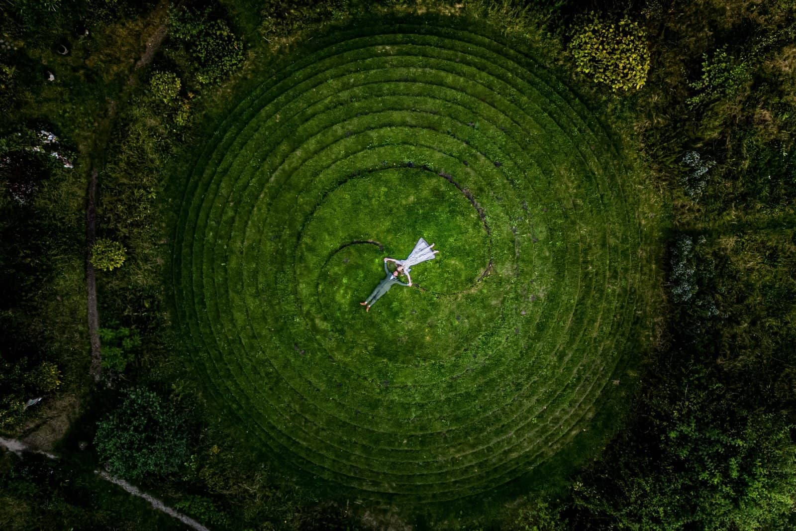 Drone photo of a couple lying at the centre of a circular grass maze