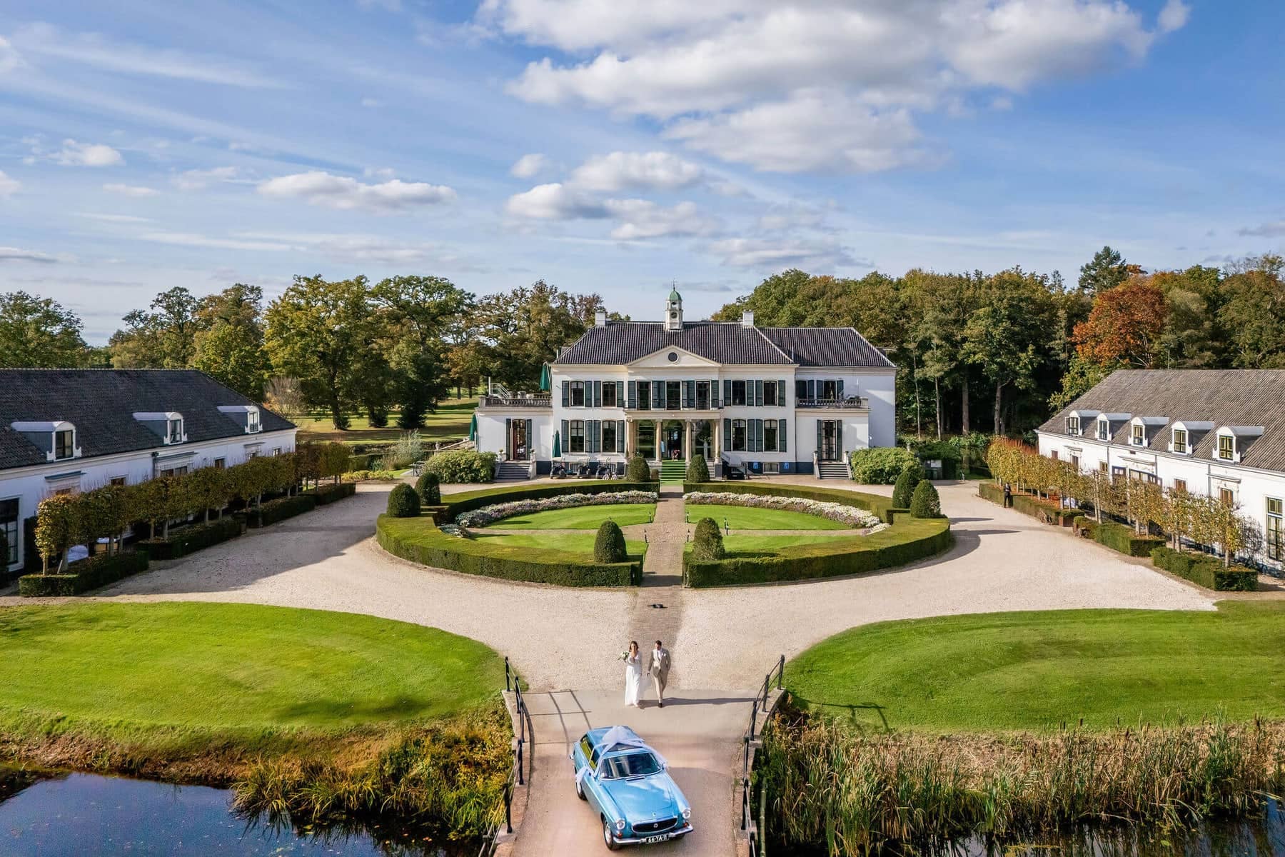 Drone photo of an estate with a blue classic car and the couple on the driveway