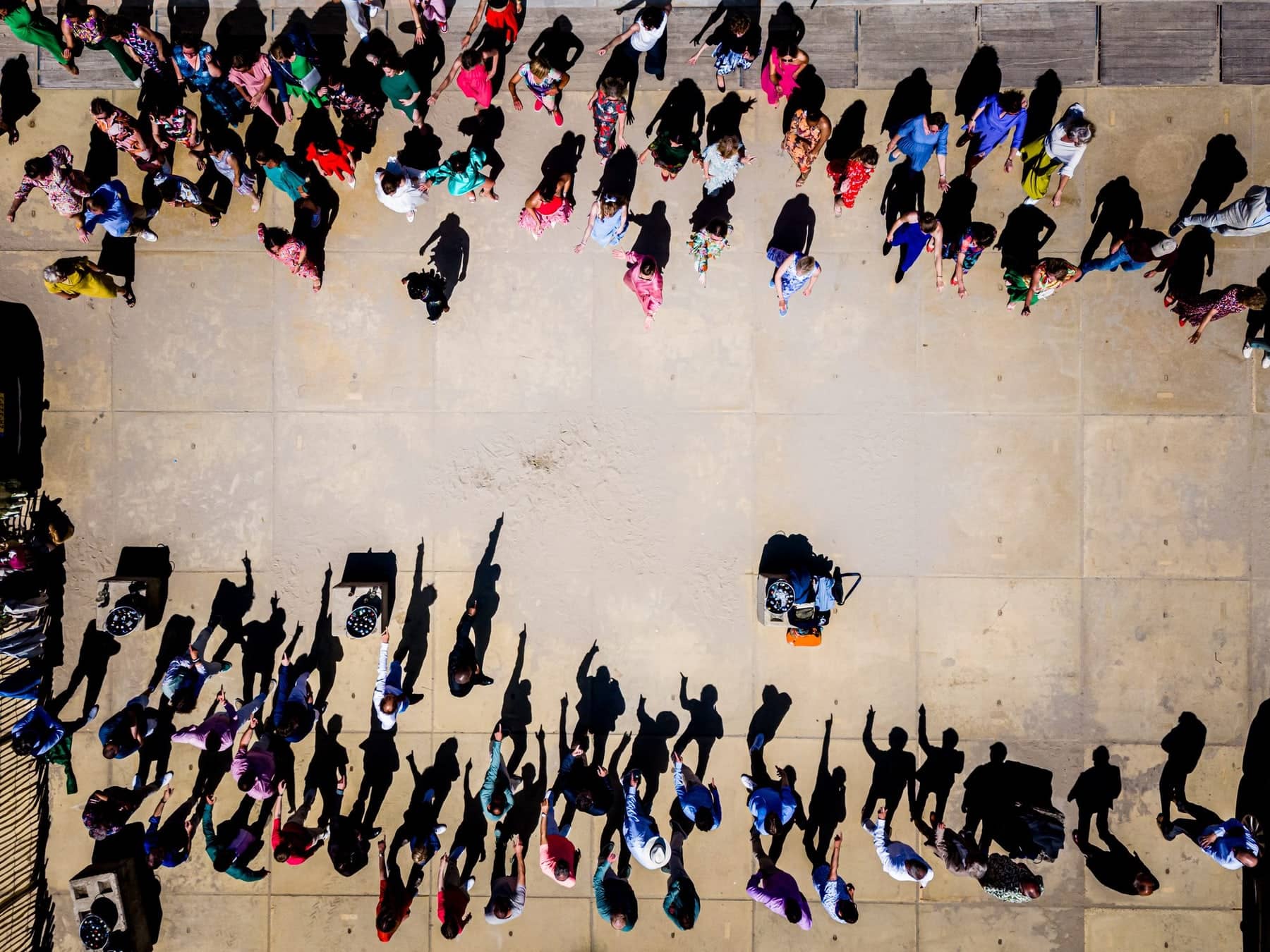 Drone shot of guests dancing on a square, casting long shadows in the late sun