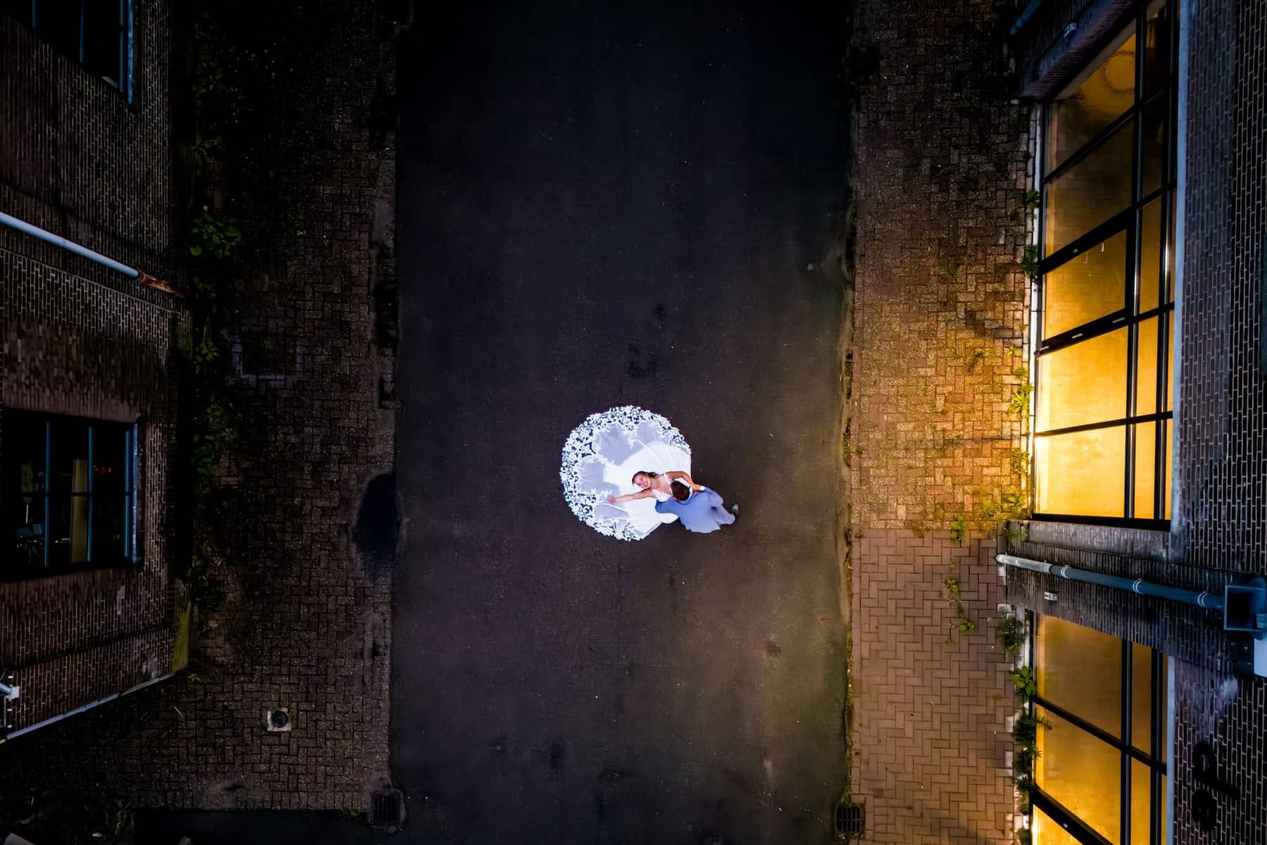 Drone shot at dusk: the couple in a narrow alley, the lace dress a white circle