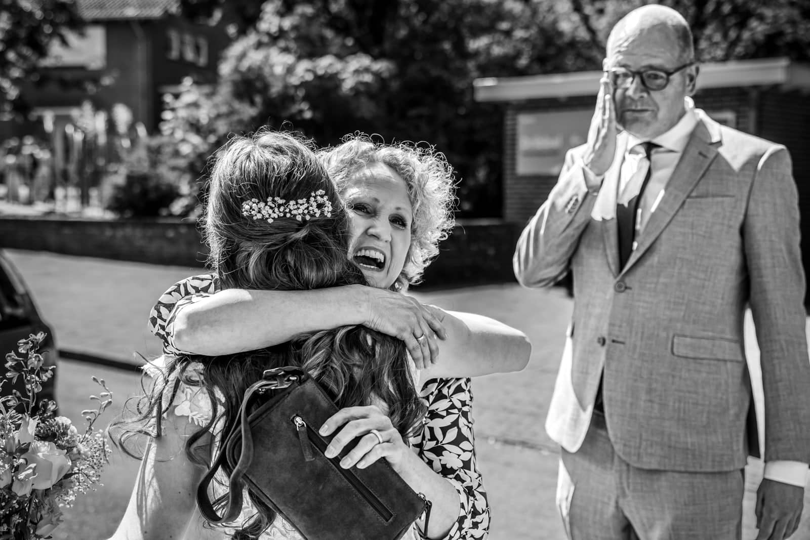 The bride gets a big hug while a man wipes away a tear (black and white)