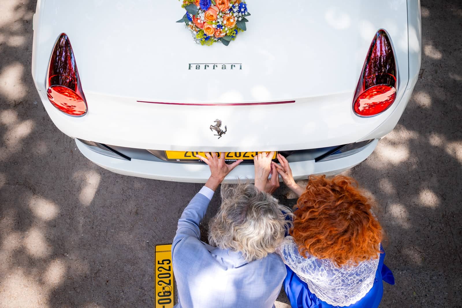 Seen from above, two guests stick a custom number plate on the couple’s white Ferrari