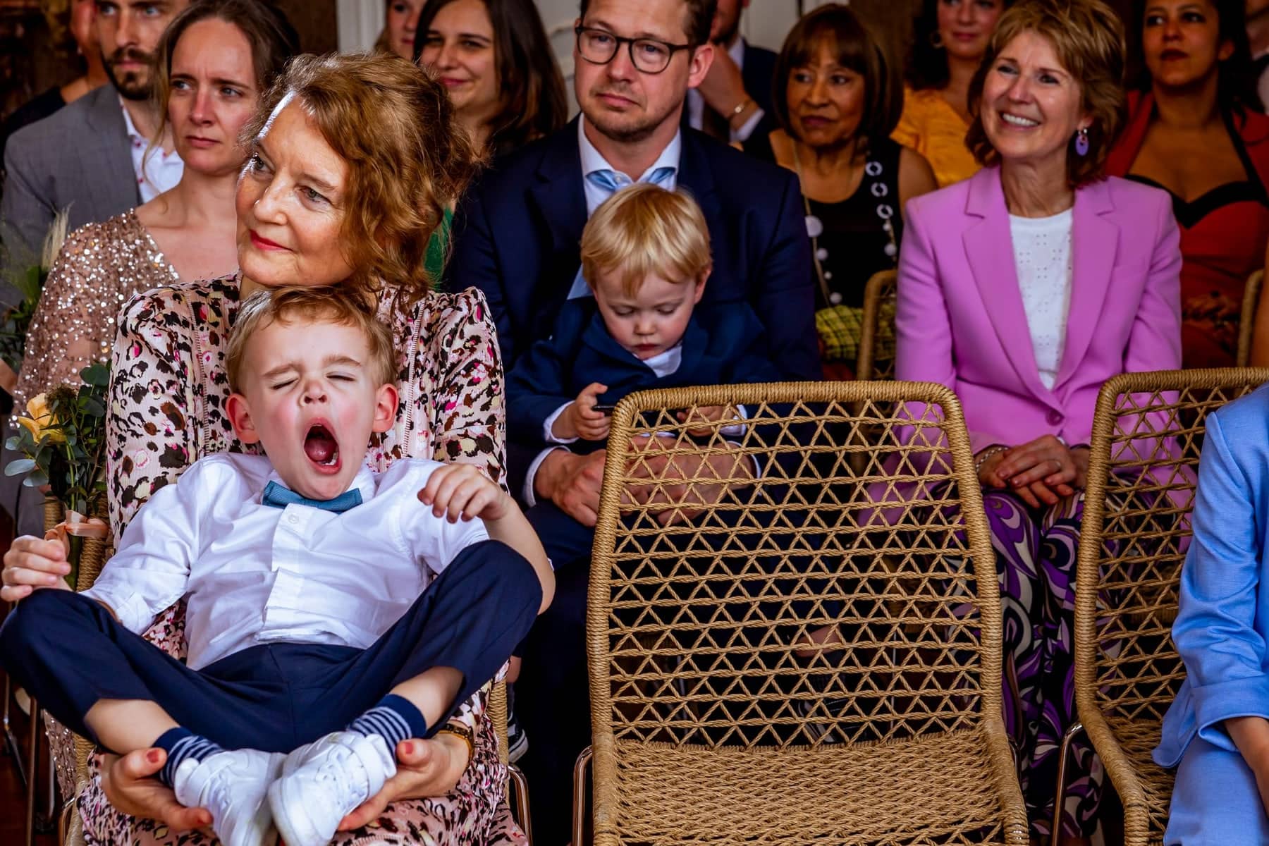 A little boy yawns widely on a lap during the ceremony