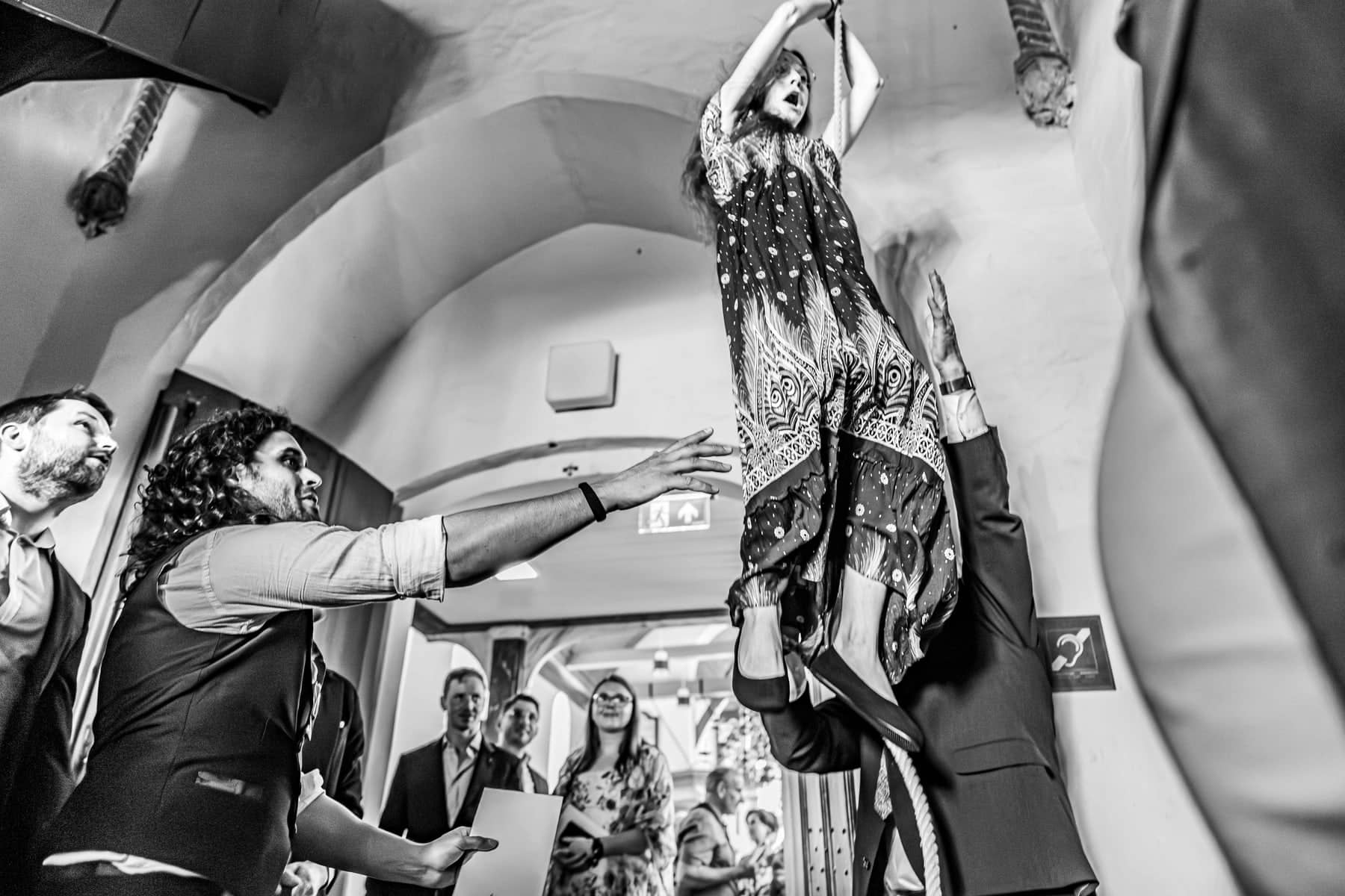 From below: a guest is lifted high into the air beneath a vaulted ceiling (black and white)