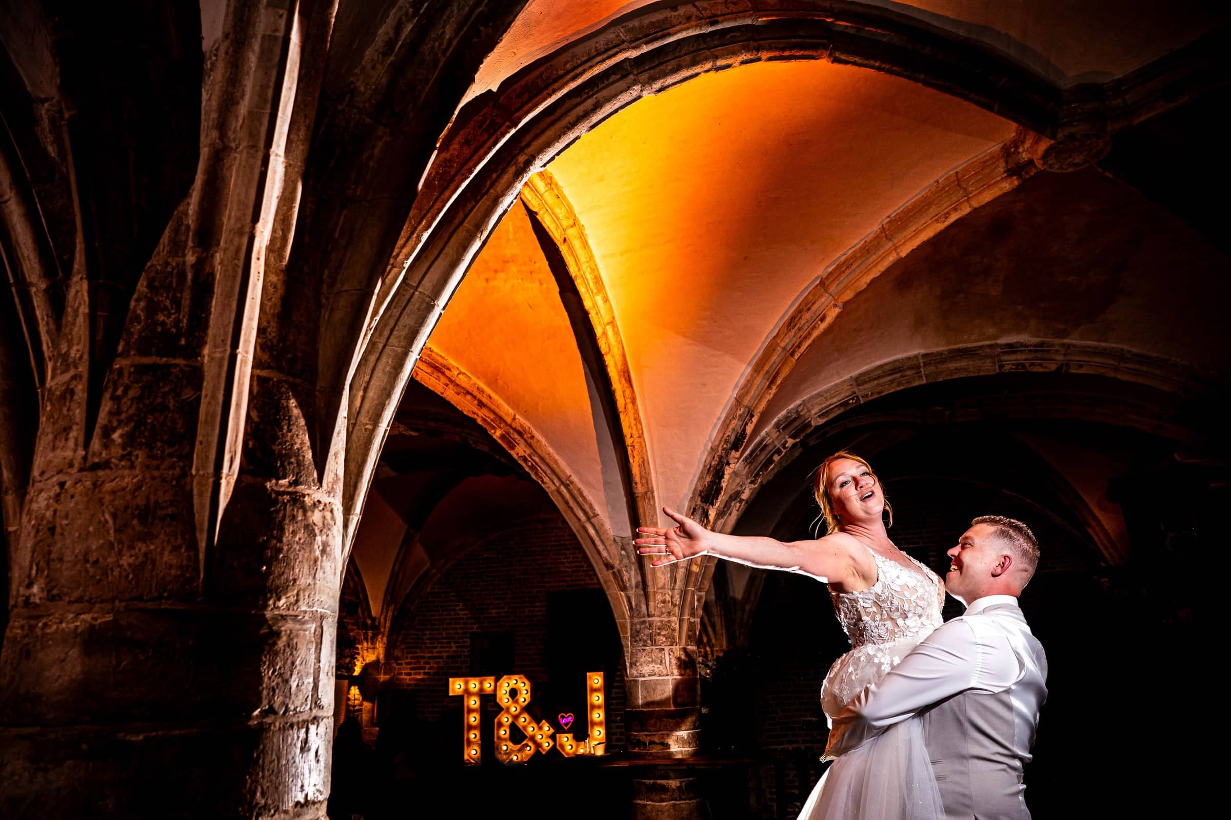 Couple dancing under an illuminated vaulted ceiling, beside light-up letters of their initials