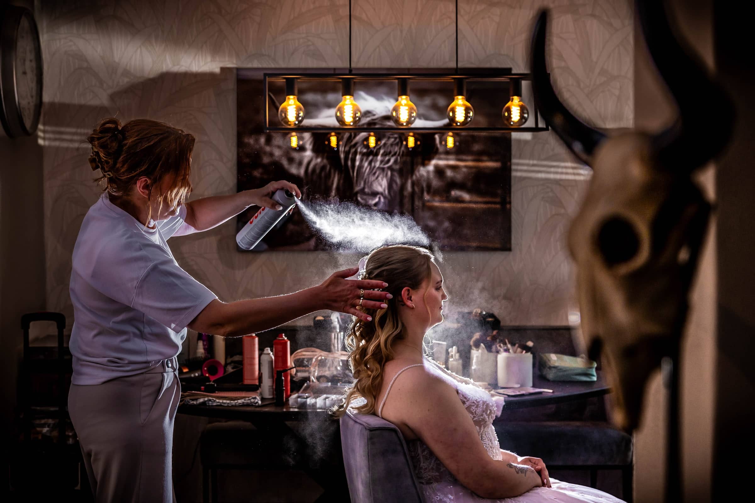 The stylist fixes the bride’s hair in a cloud of hairspray
