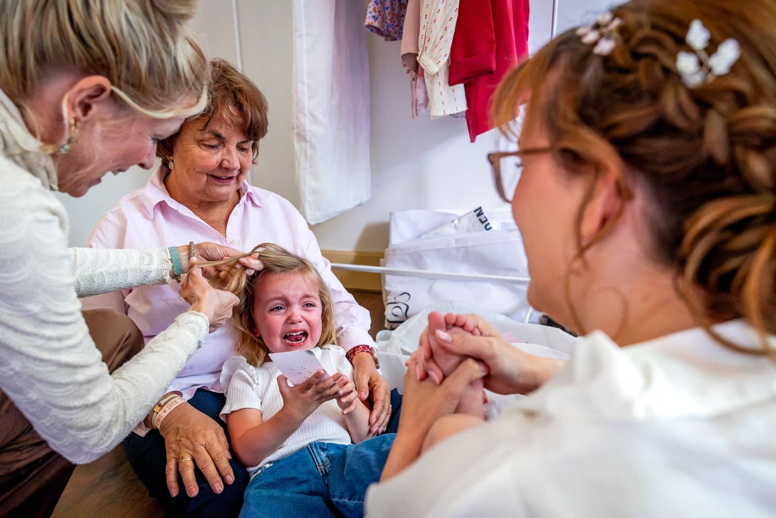 A crying girl has her hair done while the bride holds her hand to comfort her