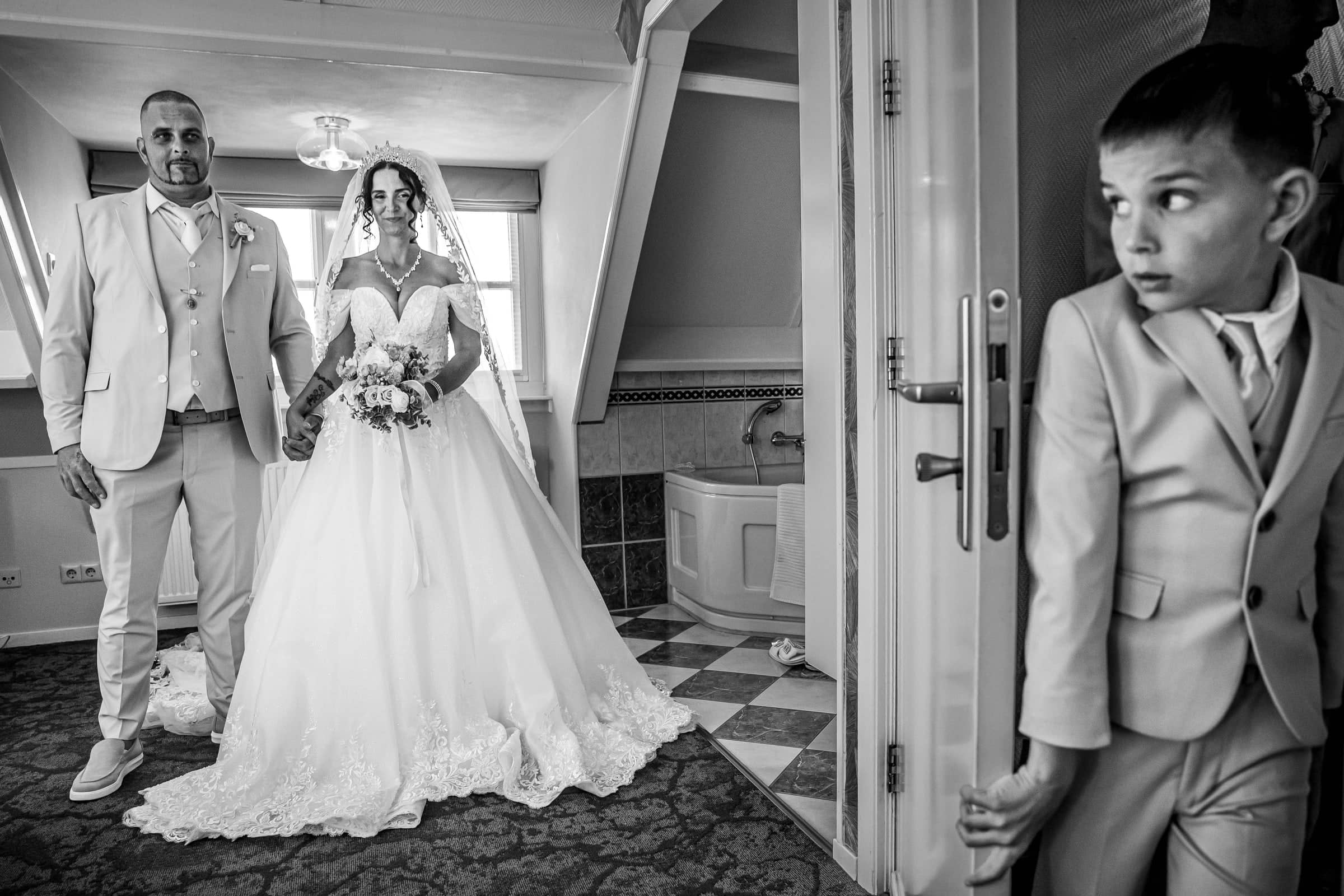 A boy peeks around the door at the bride and groom (black and white)