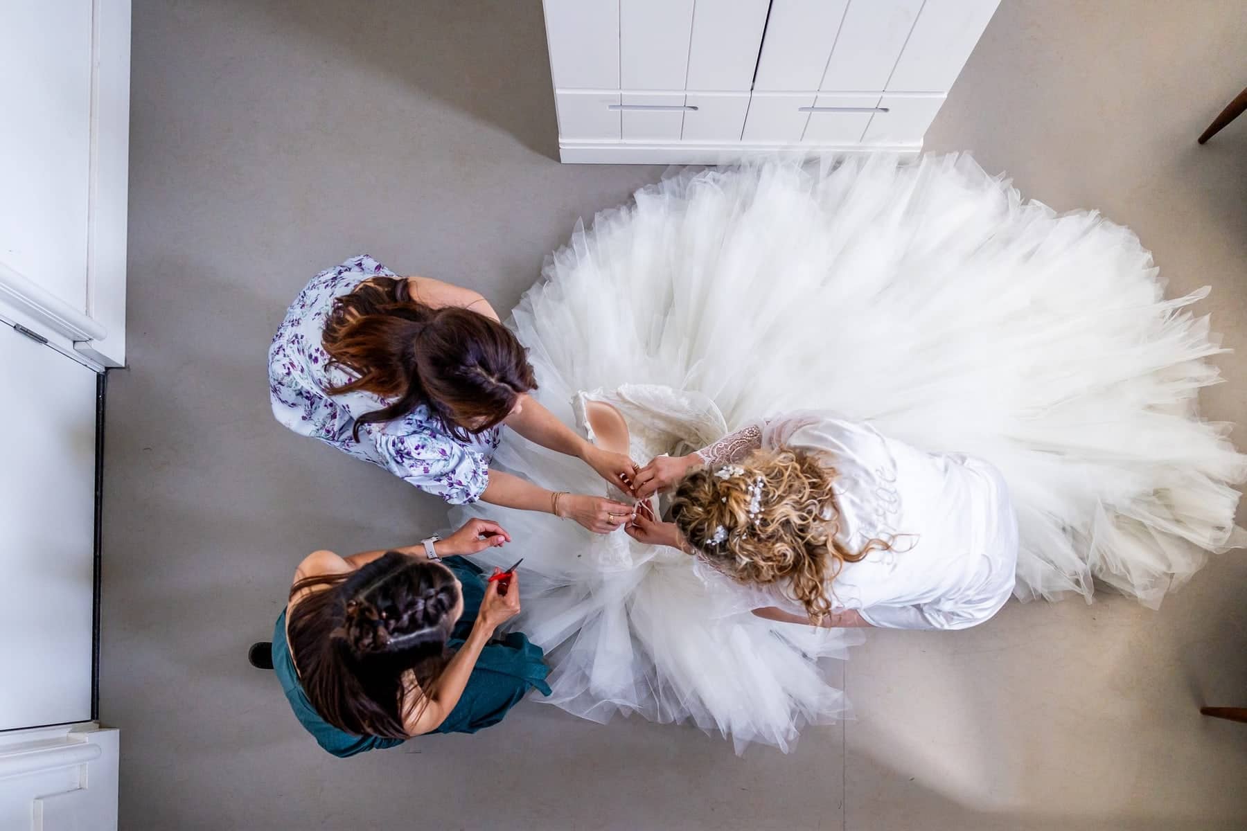 From above: friends lace up the bride’s dress, the tulle filling the floor