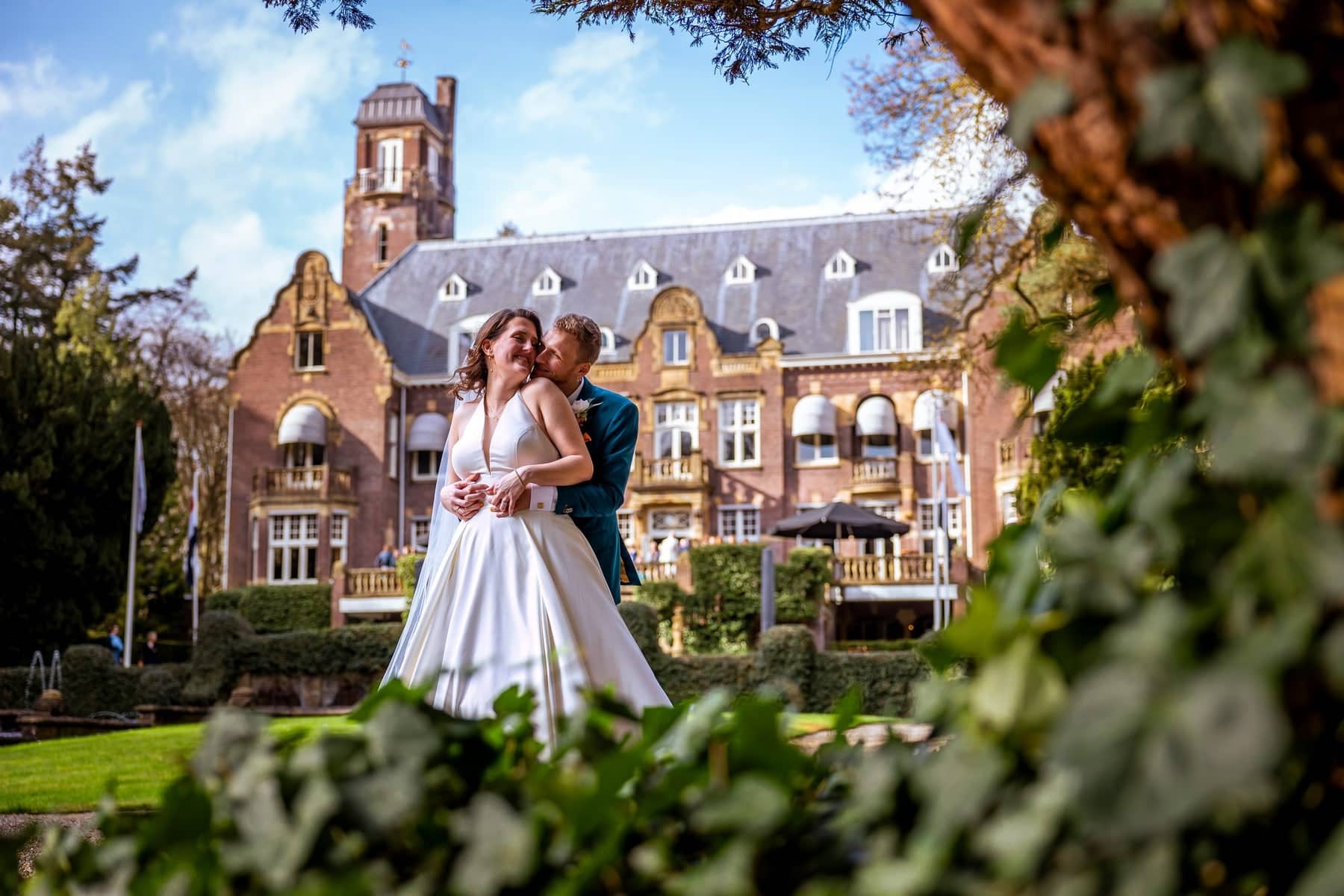 The couple embracing in front of a castle-like hotel, framed by ivy