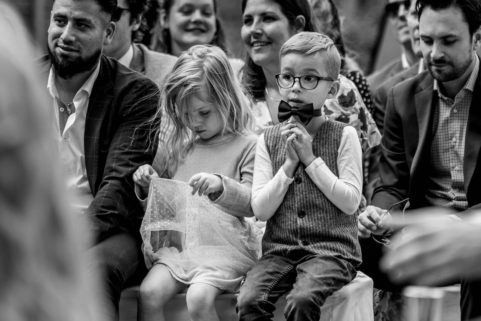 A little boy with glasses and a bow tie clasps his hands during the ceremony (black and white)