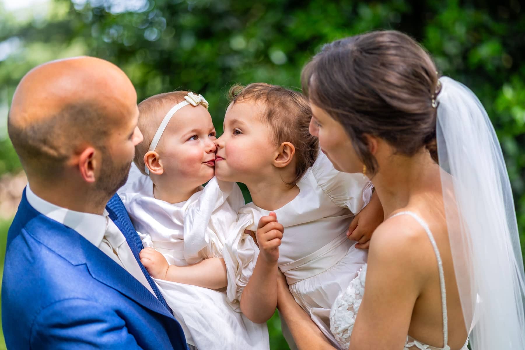 Two little girls kiss each other in the arms of the couple