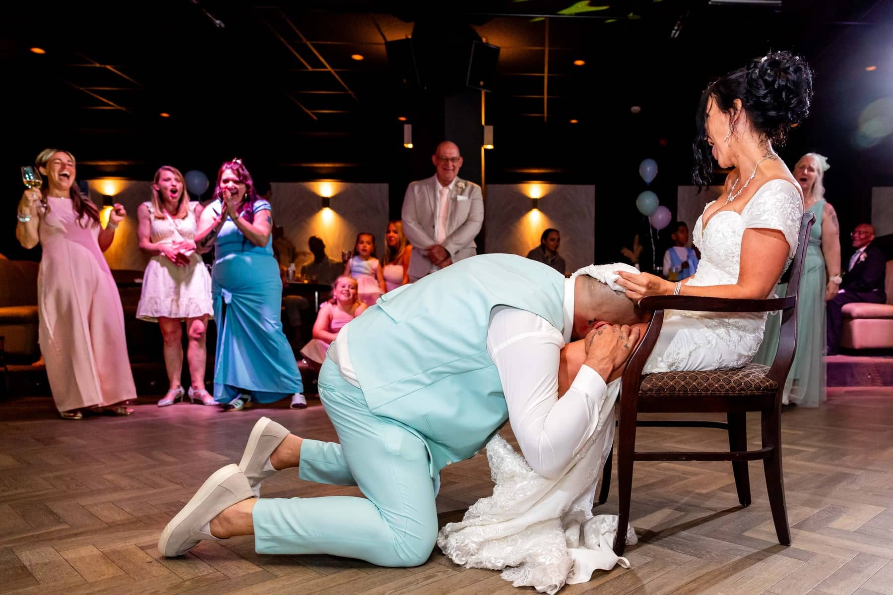 The groom dives under the dress for the garter as friends crack up