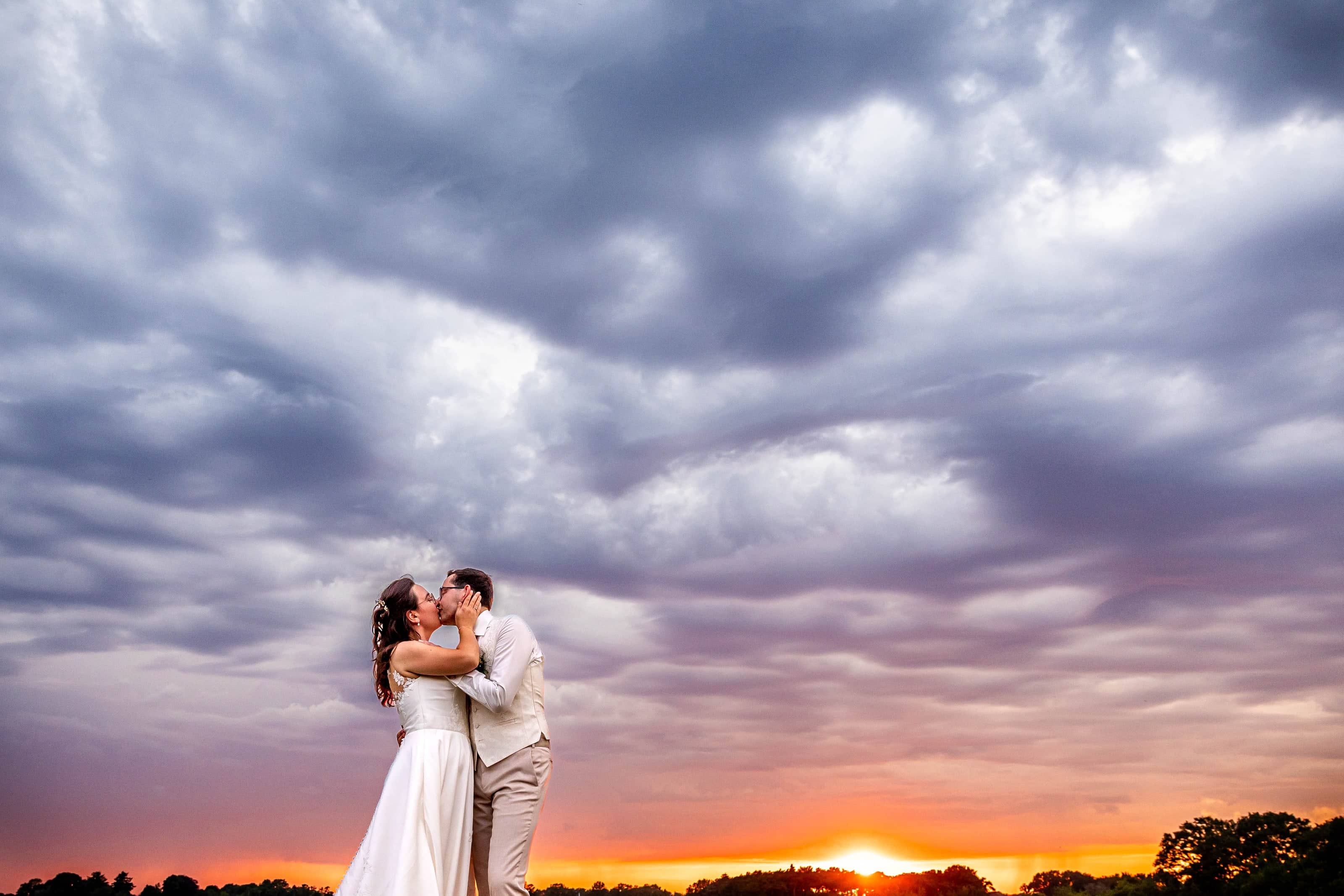 Couple kissing under a dramatic cloudy sky as the sun sets