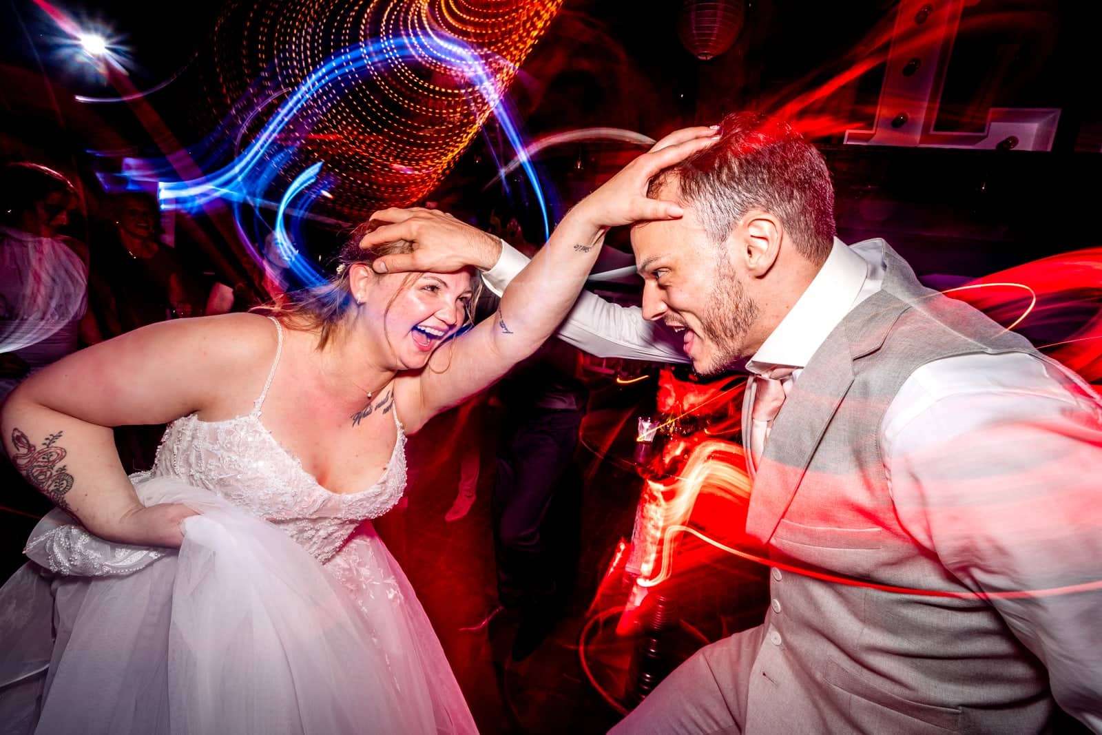 Bride and groom dance wildly between red and blue light trails