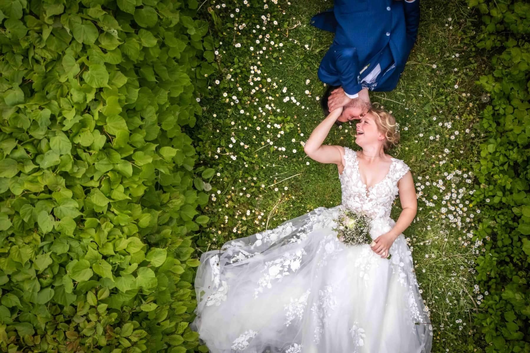 From above: the bride lies among the daisies while the groom kisses her hand