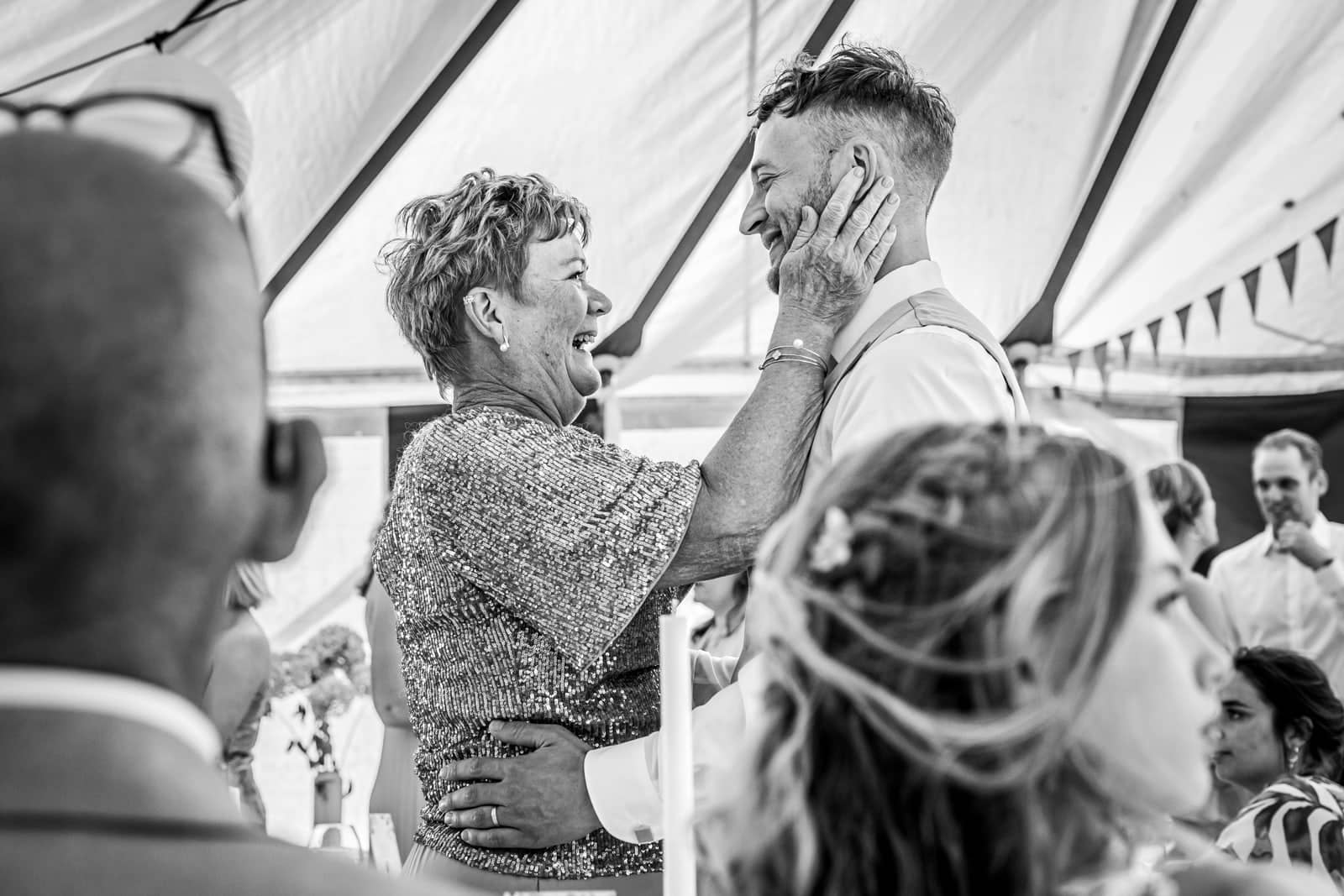 A mother laughingly holds the groom’s face (black and white)