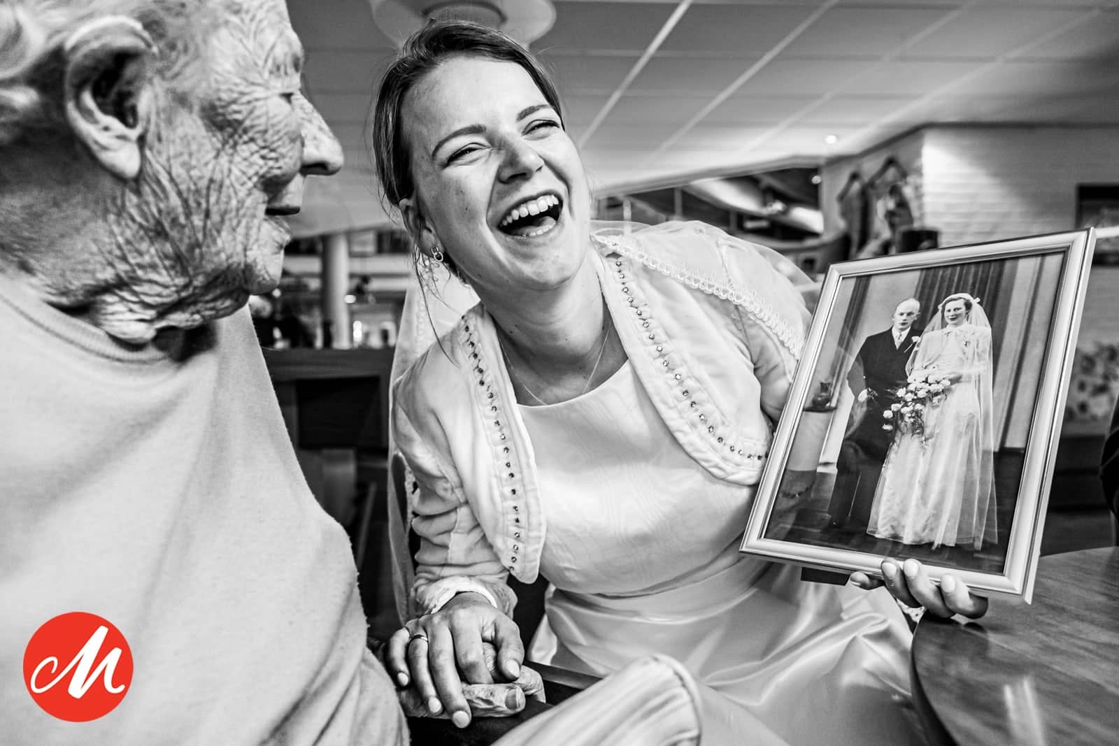 The bride laughs with an elderly man while holding a framed old wedding photo (black and white)
