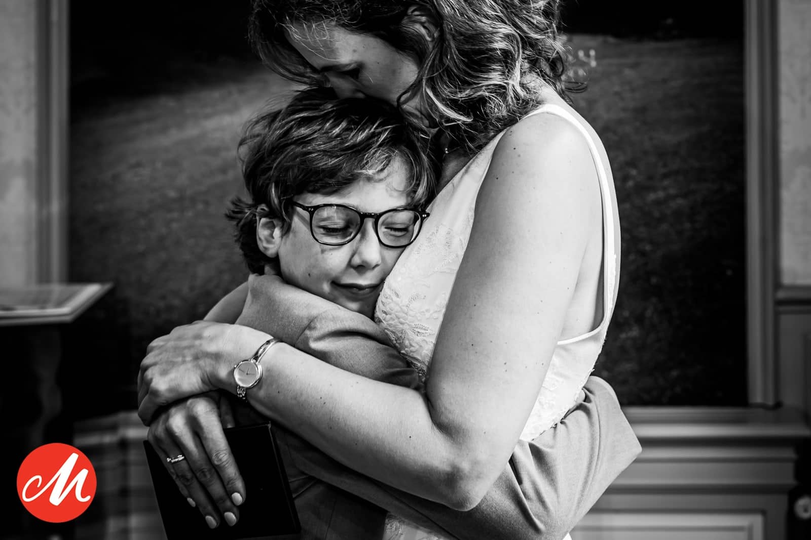 A boy with glasses closes his eyes in the bride’s embrace (black and white)