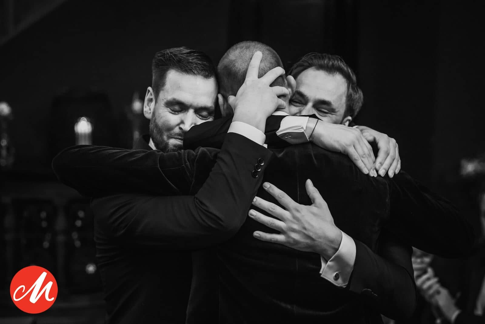 Three men in suits share an emotional hug (black and white)