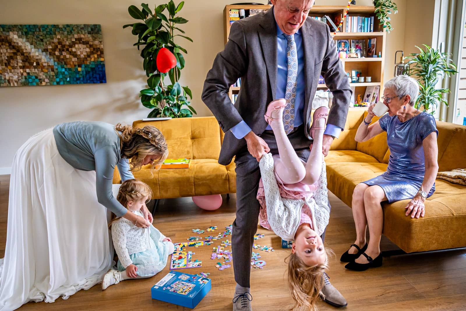 Chaos in the living room: a man holds a girl upside down while the bride helps a toddler
