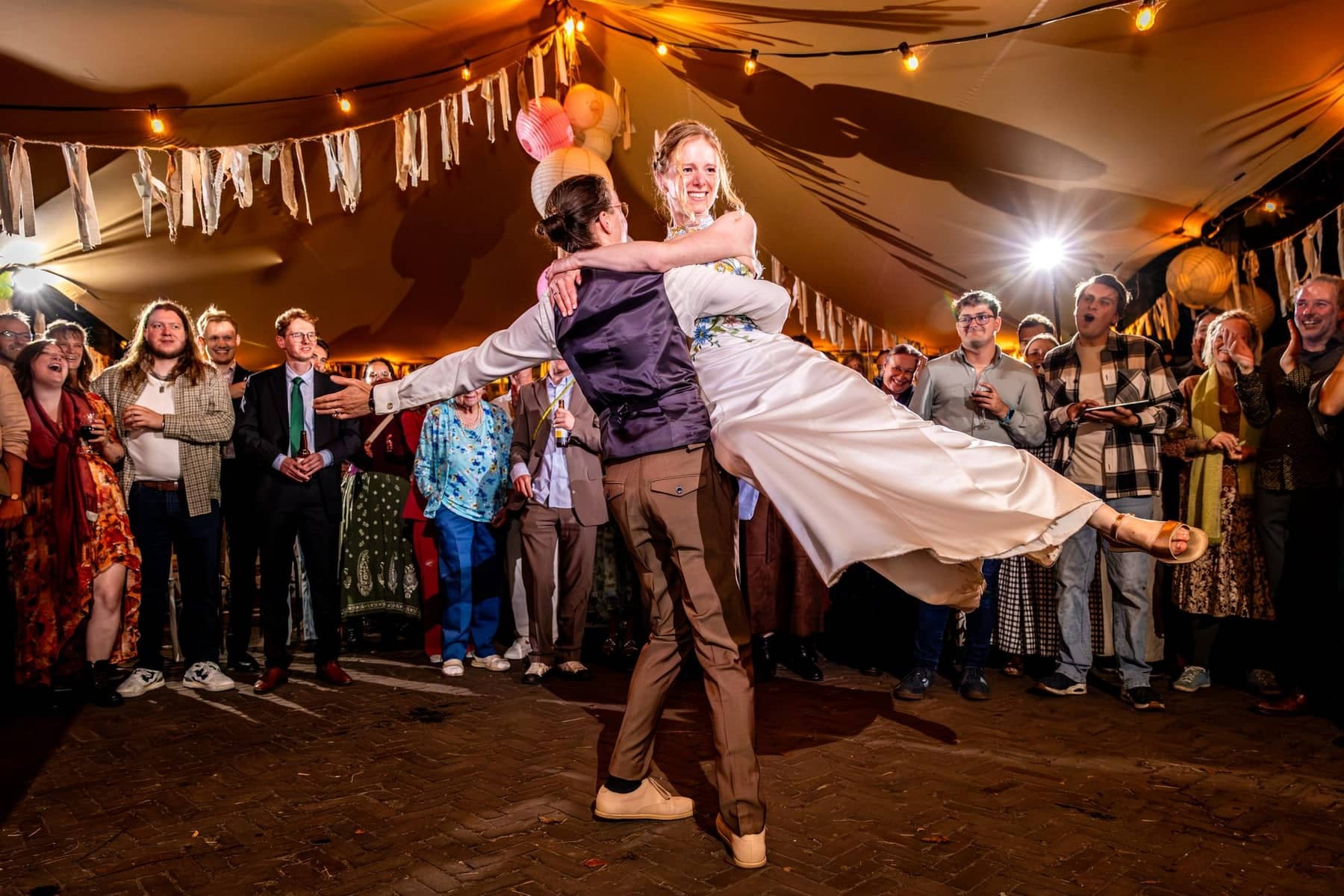The groom lifts the bride high during the first dance in a party tent full of lights and bunting