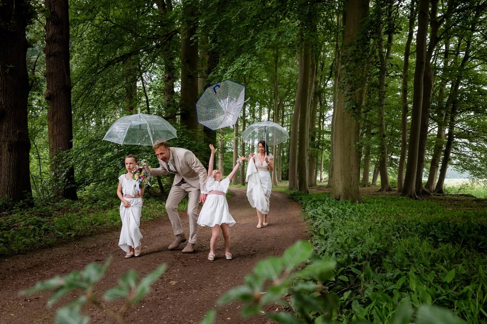 The couple and two girls skip along a forest path with clear umbrellas