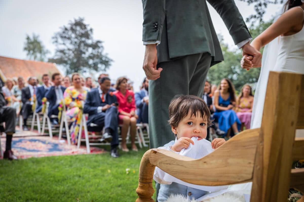 A toddler peeks over a chair as the couple walk past during the garden ceremony