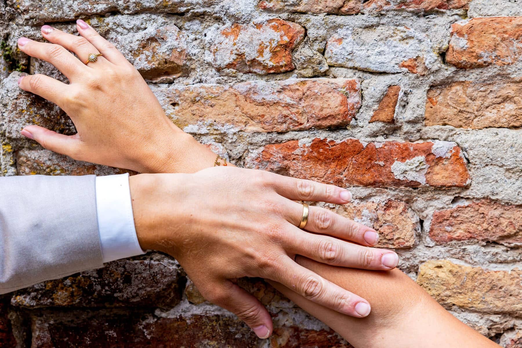 Hands with wedding rings against an old brick wall