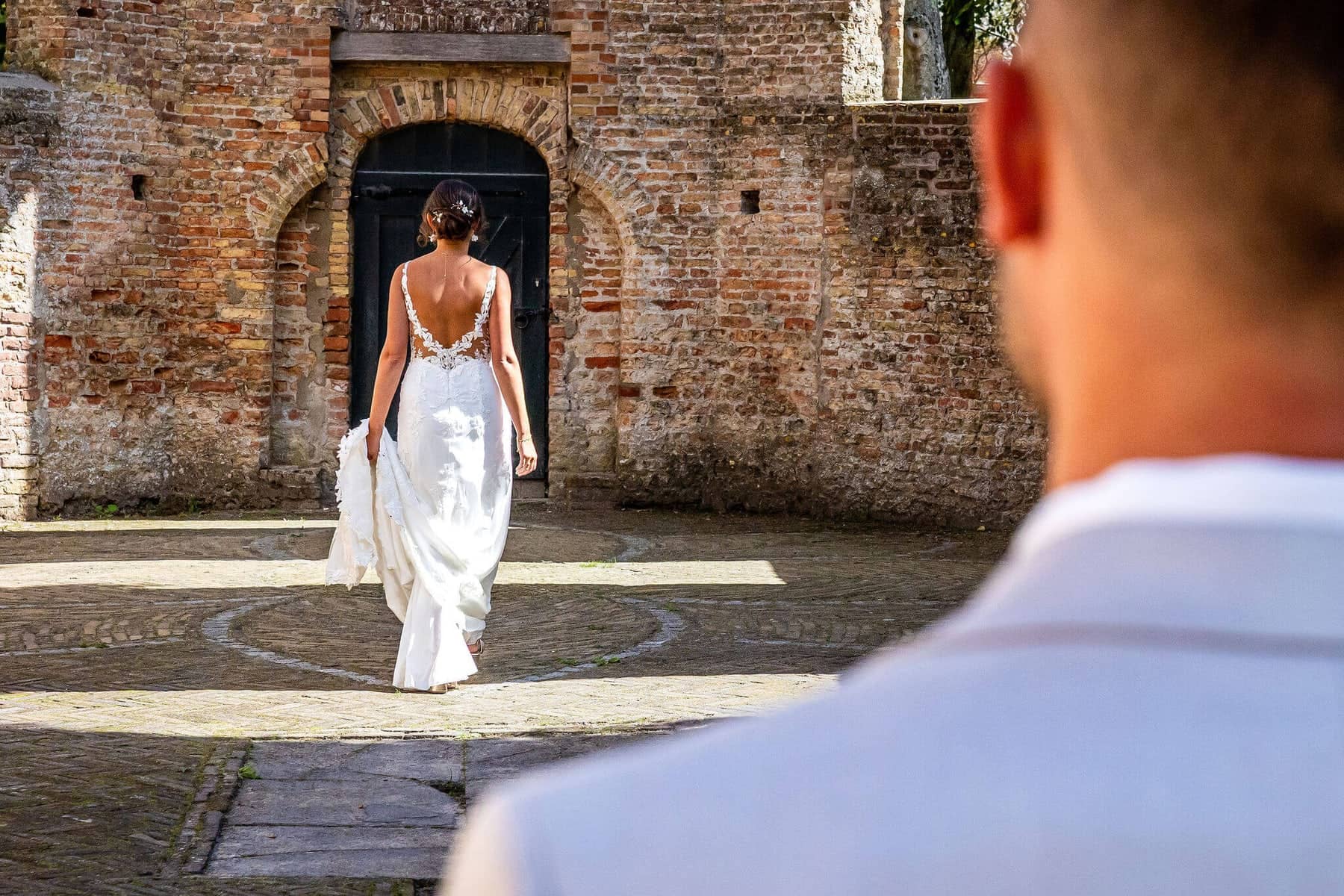 The bride walks across the courtyard of an old ruin, with the groom in the foreground