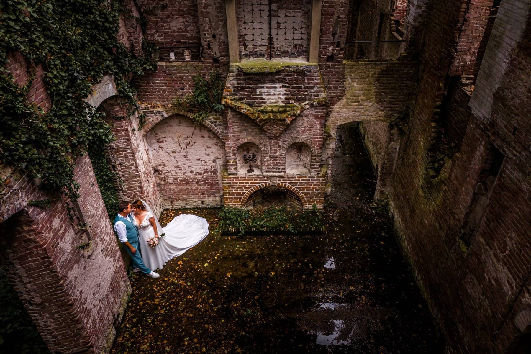 The couple in an overgrown brick ruin, the train of the dress across the ground
