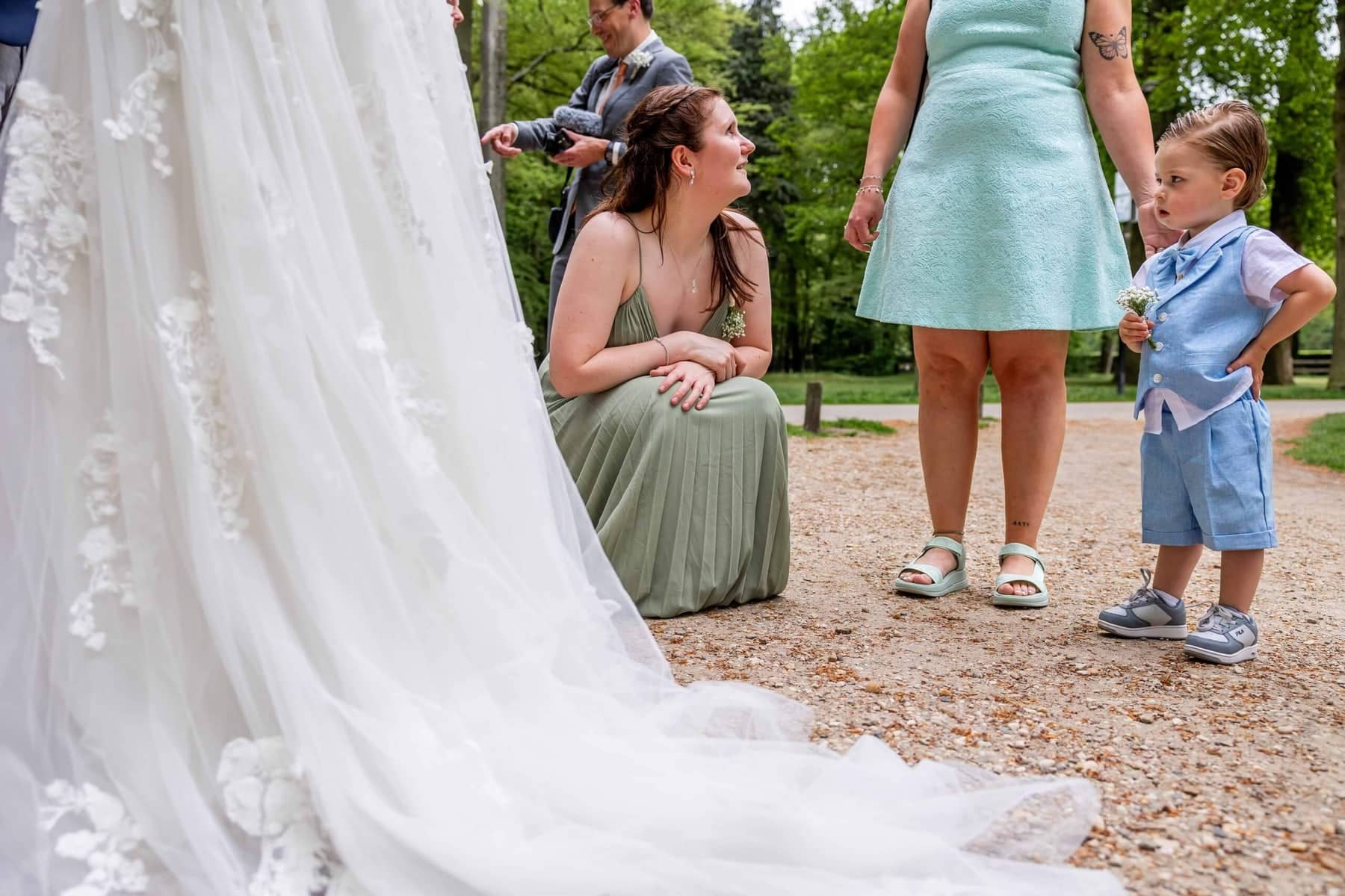 The train of the wedding dress in the foreground, with guests and a little boy on the gravel