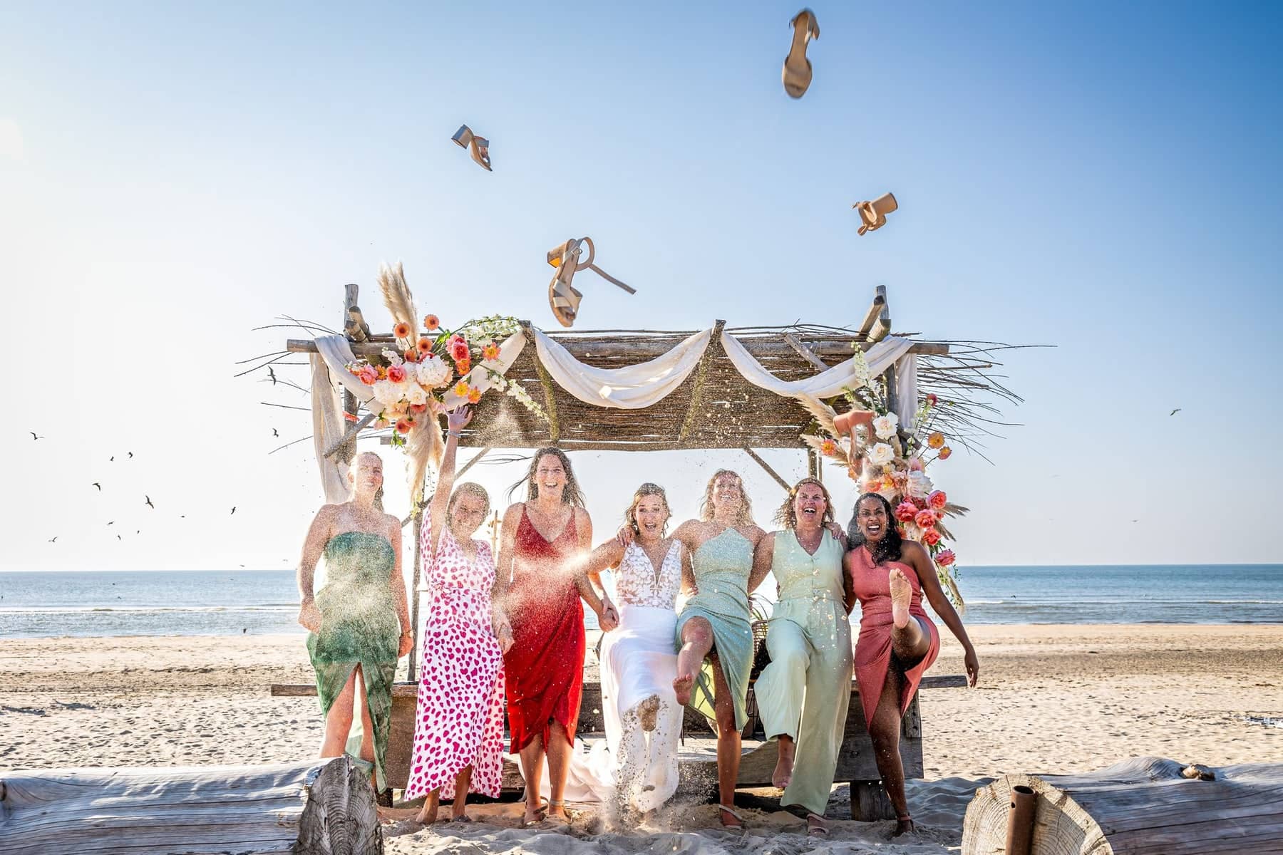 The bride and bridesmaids throw their shoes into the air at a beach ceremony