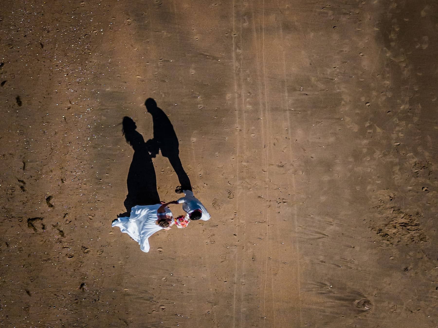 Drone photo of a couple hand in hand on the beach, casting long shadows