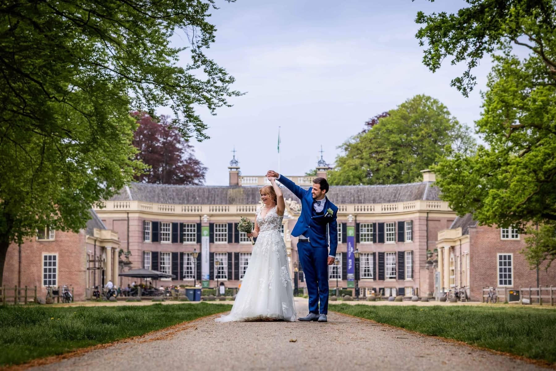 The groom twirls the bride on the drive in front of a country house