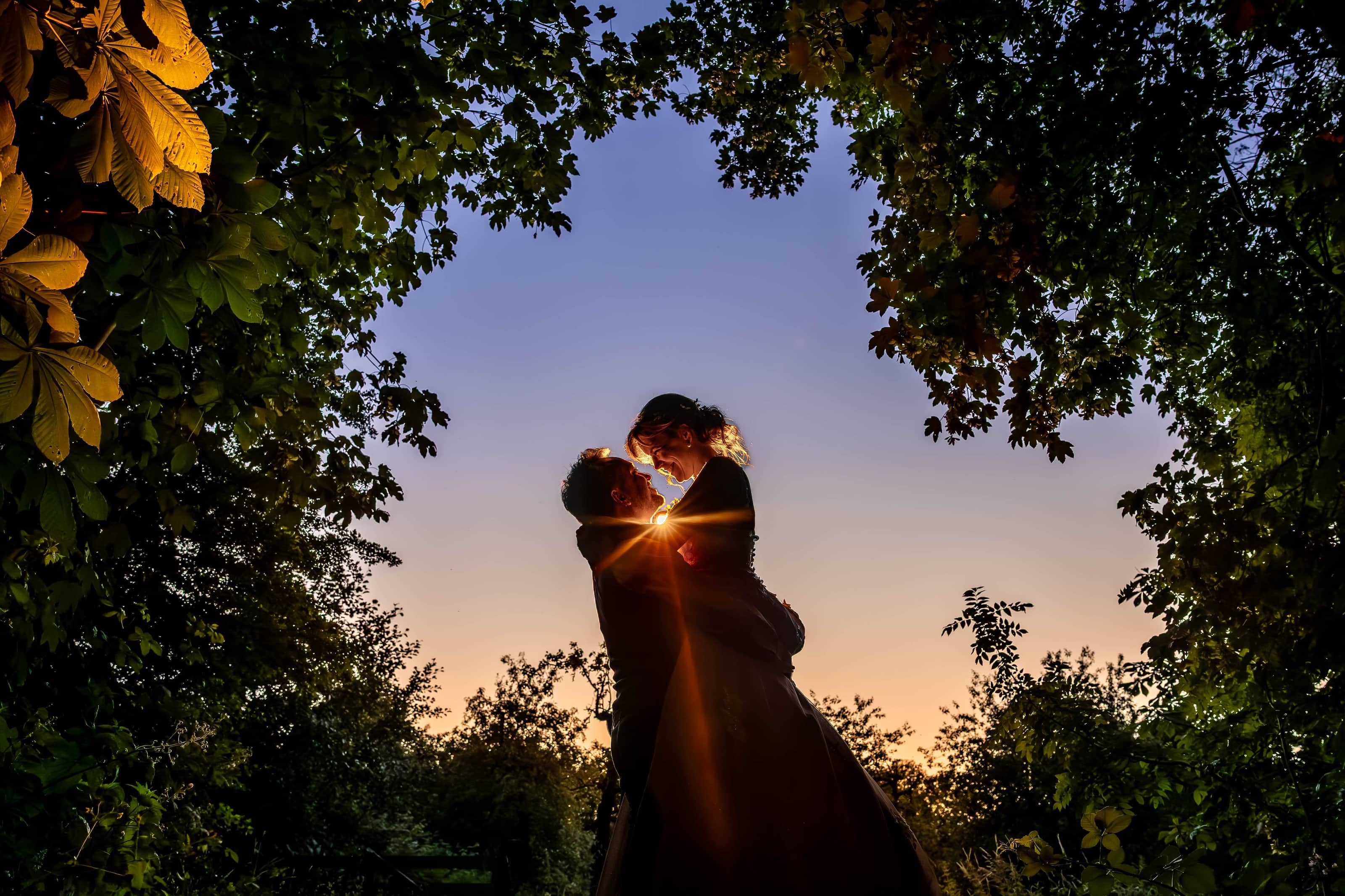 Couple kissing at sunset, framed by leaves