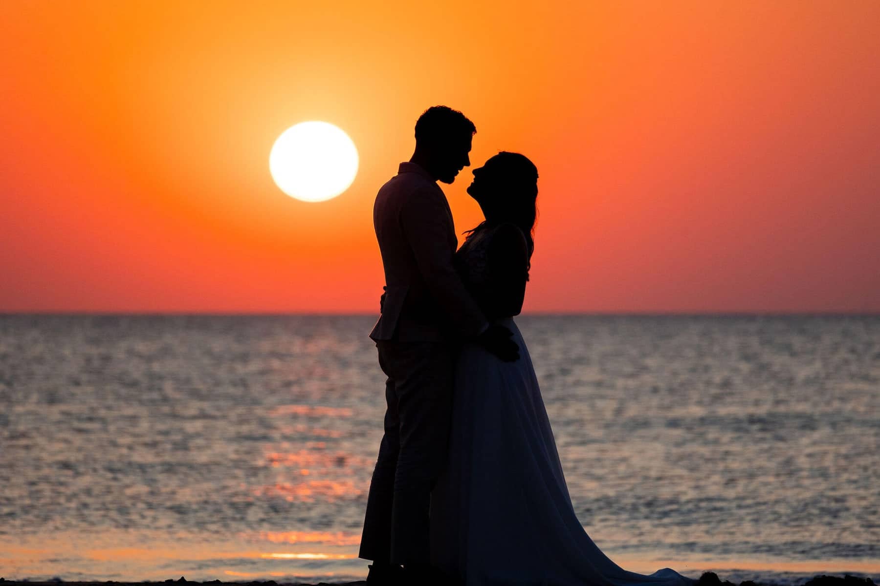 Silhouette of a couple against an orange sunset over the sea