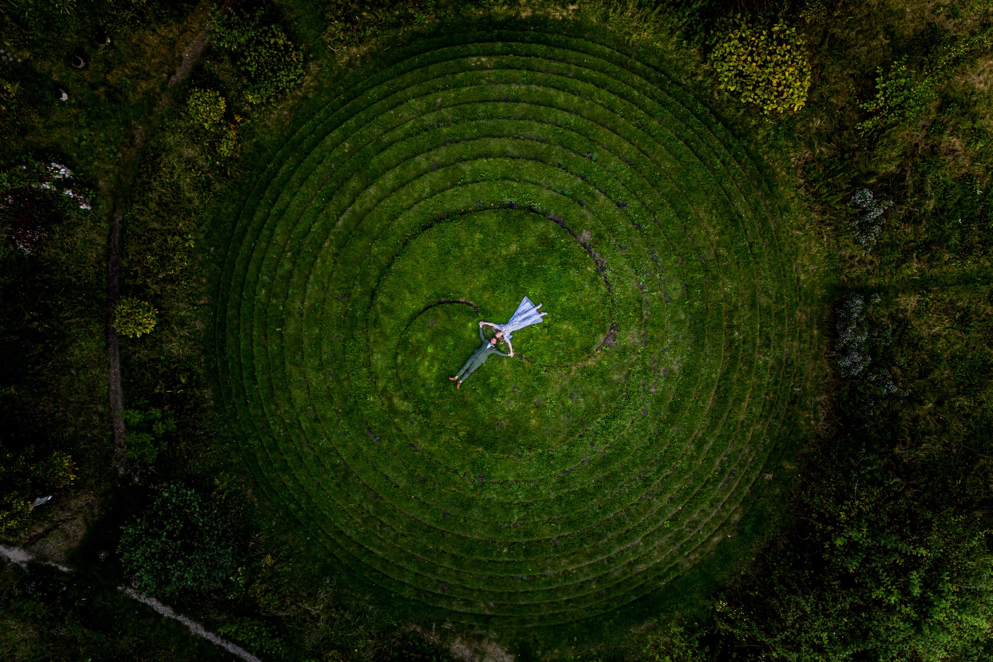 Drone shot of a couple lying in the centre of a circular grass maze
