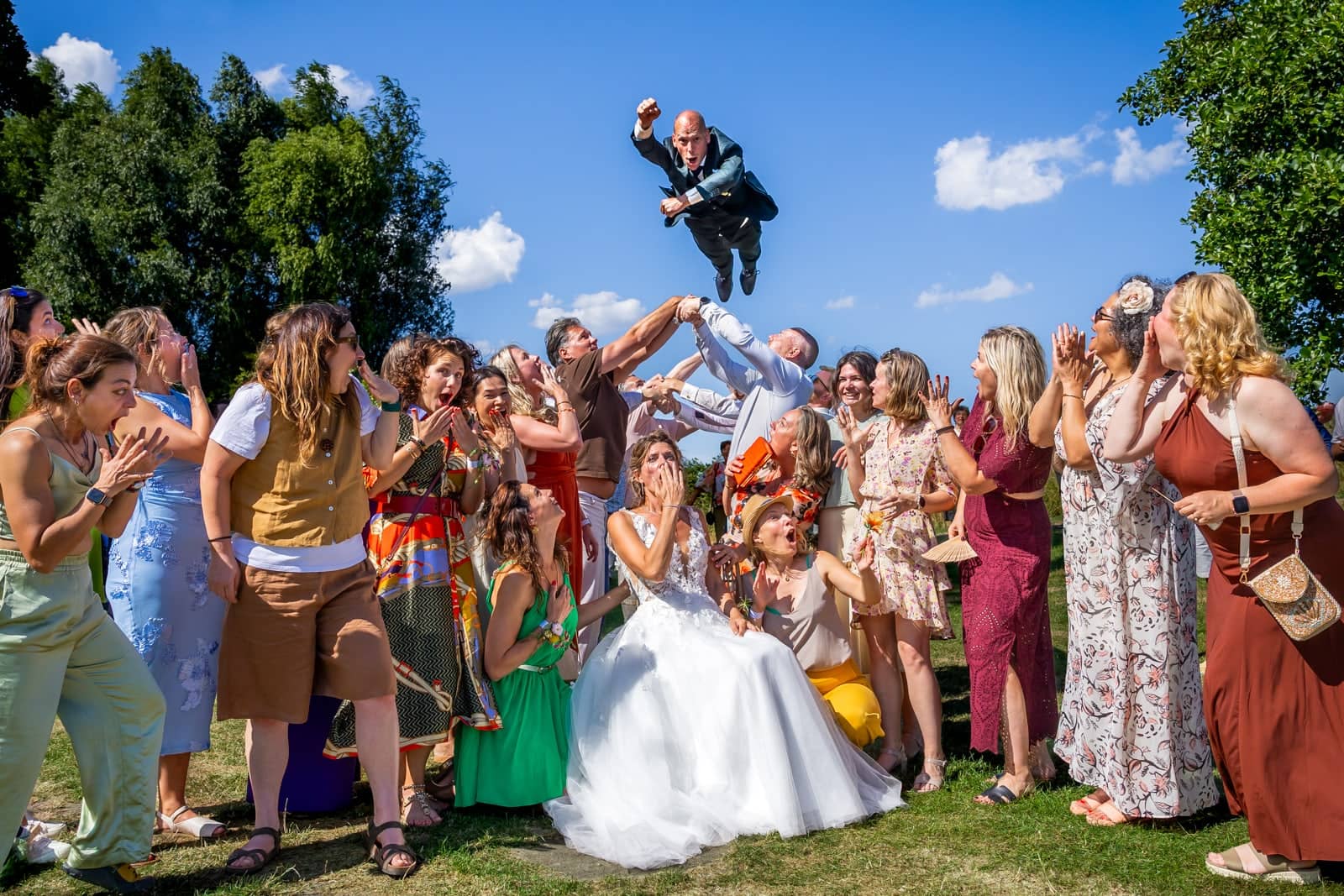 Friends throw the groom high into the air as the bride and guests cheer