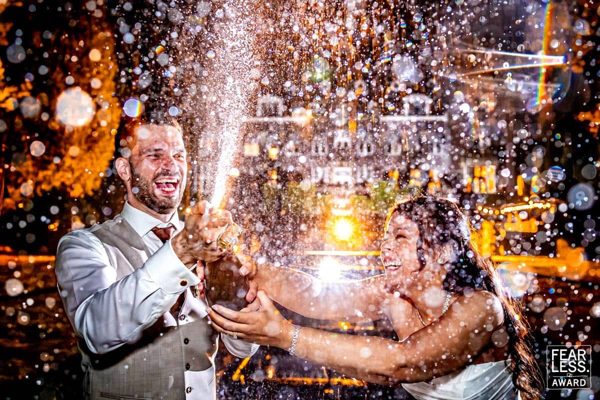 Het bruidspaar spuit lachend champagne in het avondlicht, de druppels lichten op